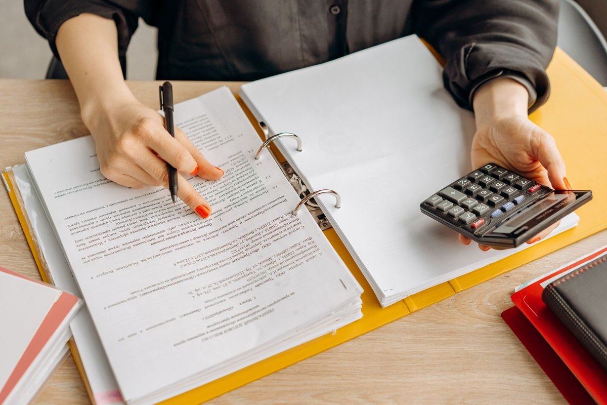 A person checking paper records by hand with a calculator